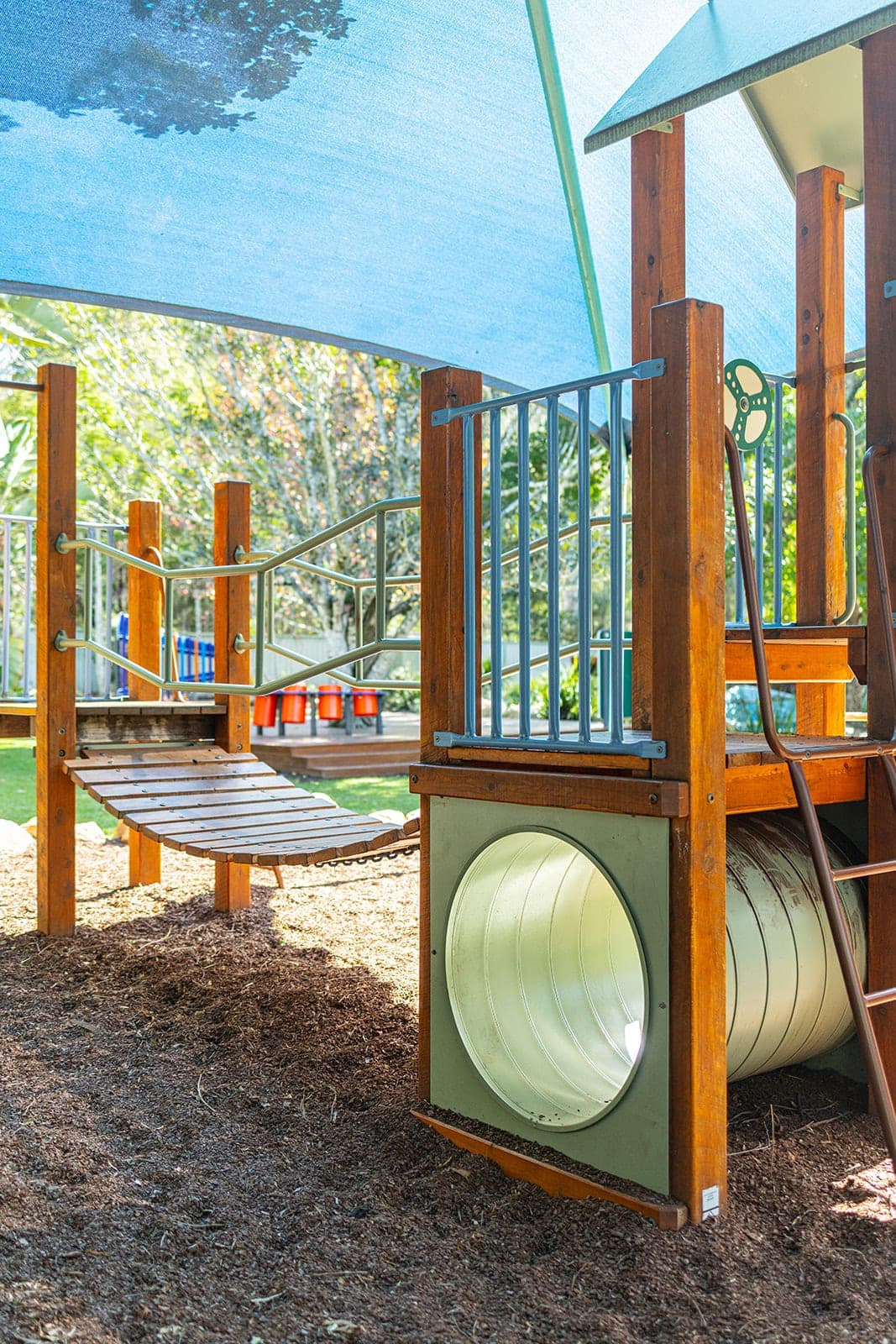 Timber climbing fort with a tunnel under a shade sail