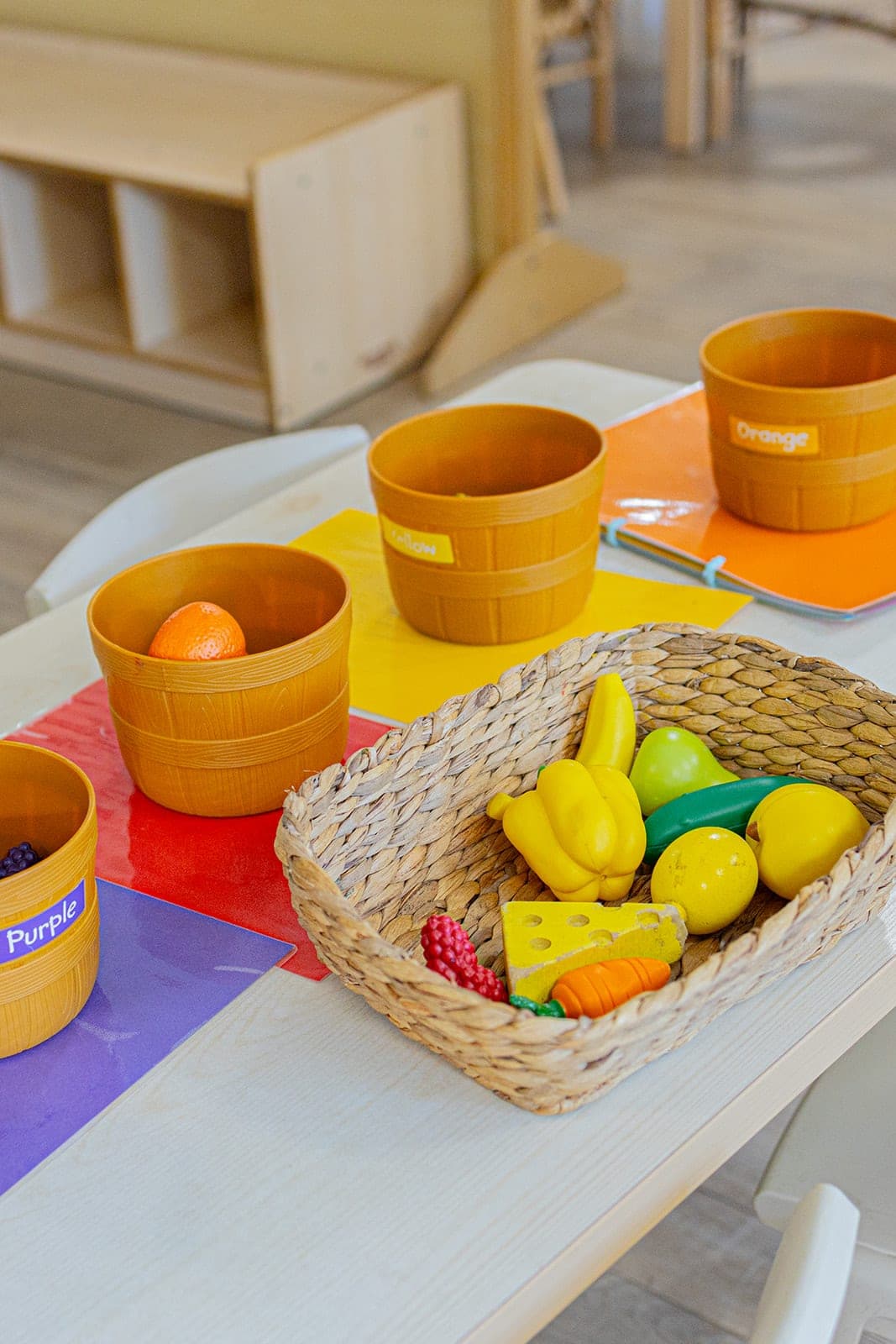 Basket of play fruit beside timber bowls on a shelf