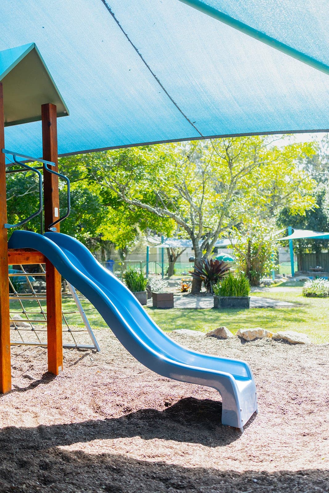 Blue slide under a shade sail surrounded by trees