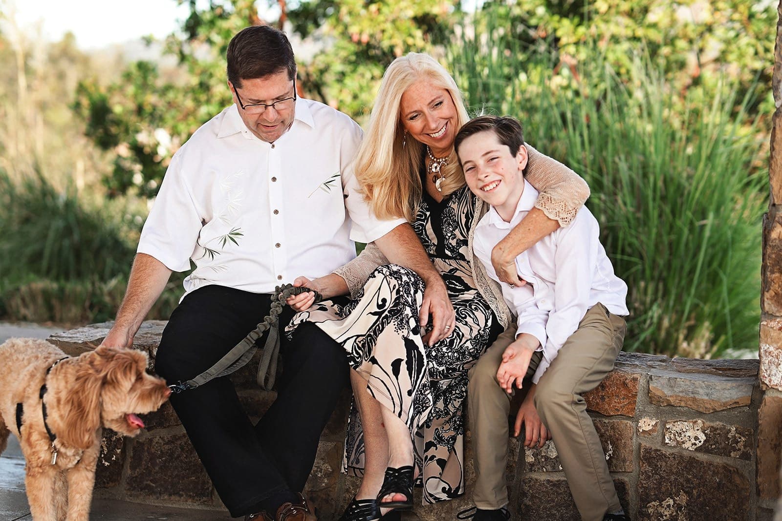 Parents and their teenage son sitting on a stone wall with their golden dog