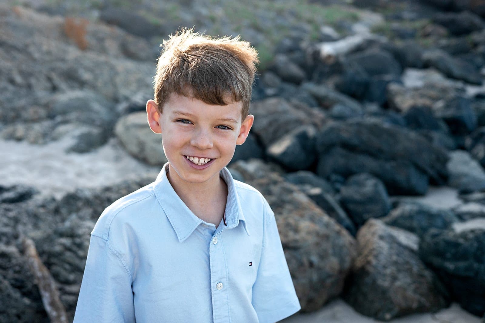 Smiling boy in a blue shirt in front of dark beach rocks