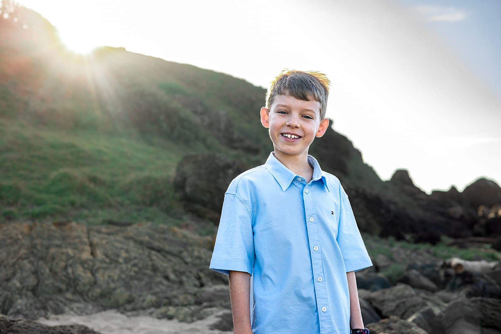 Boy grinning in golden sunlight on a grassy headland
