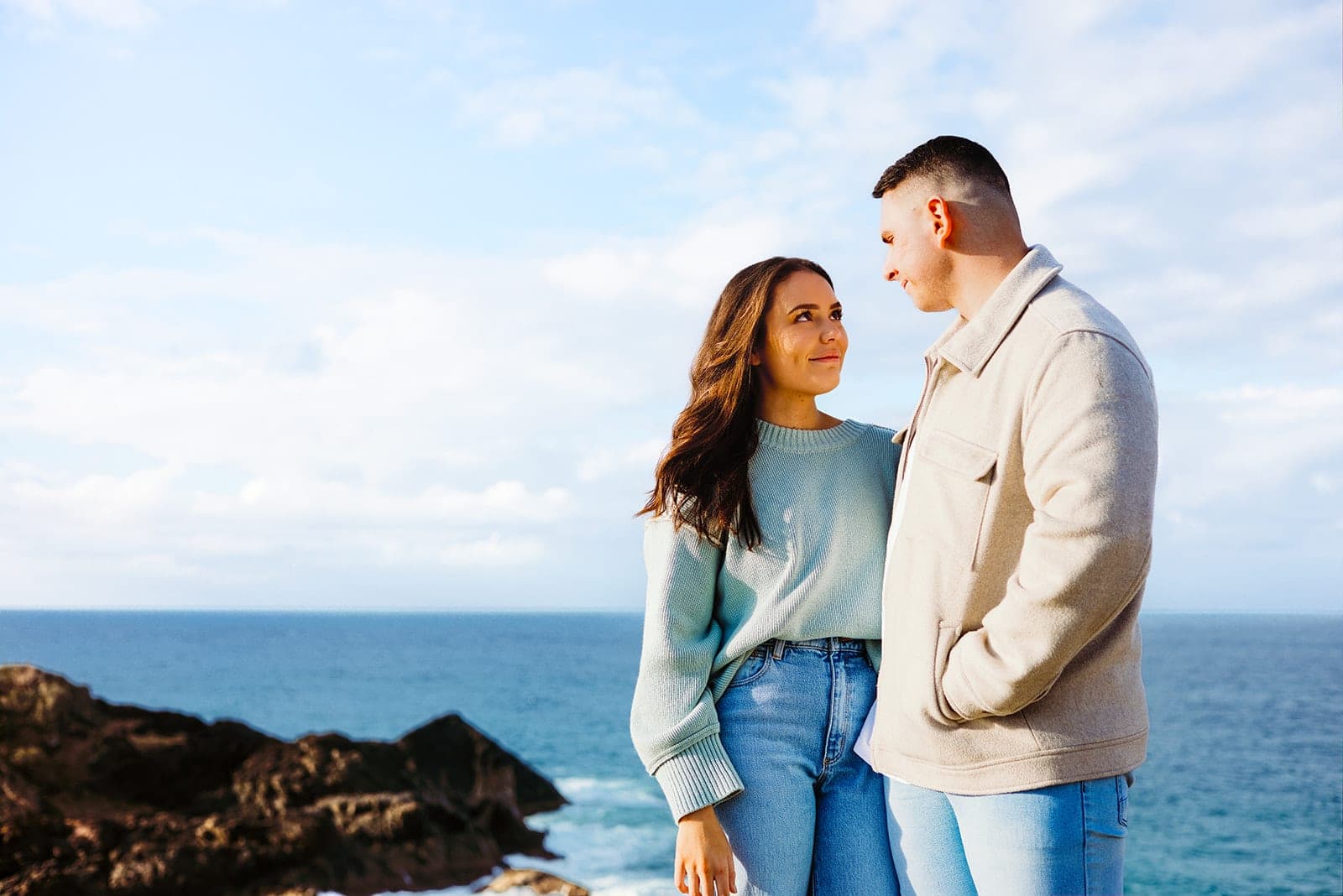 Couple looking at each other with the blue ocean behind them