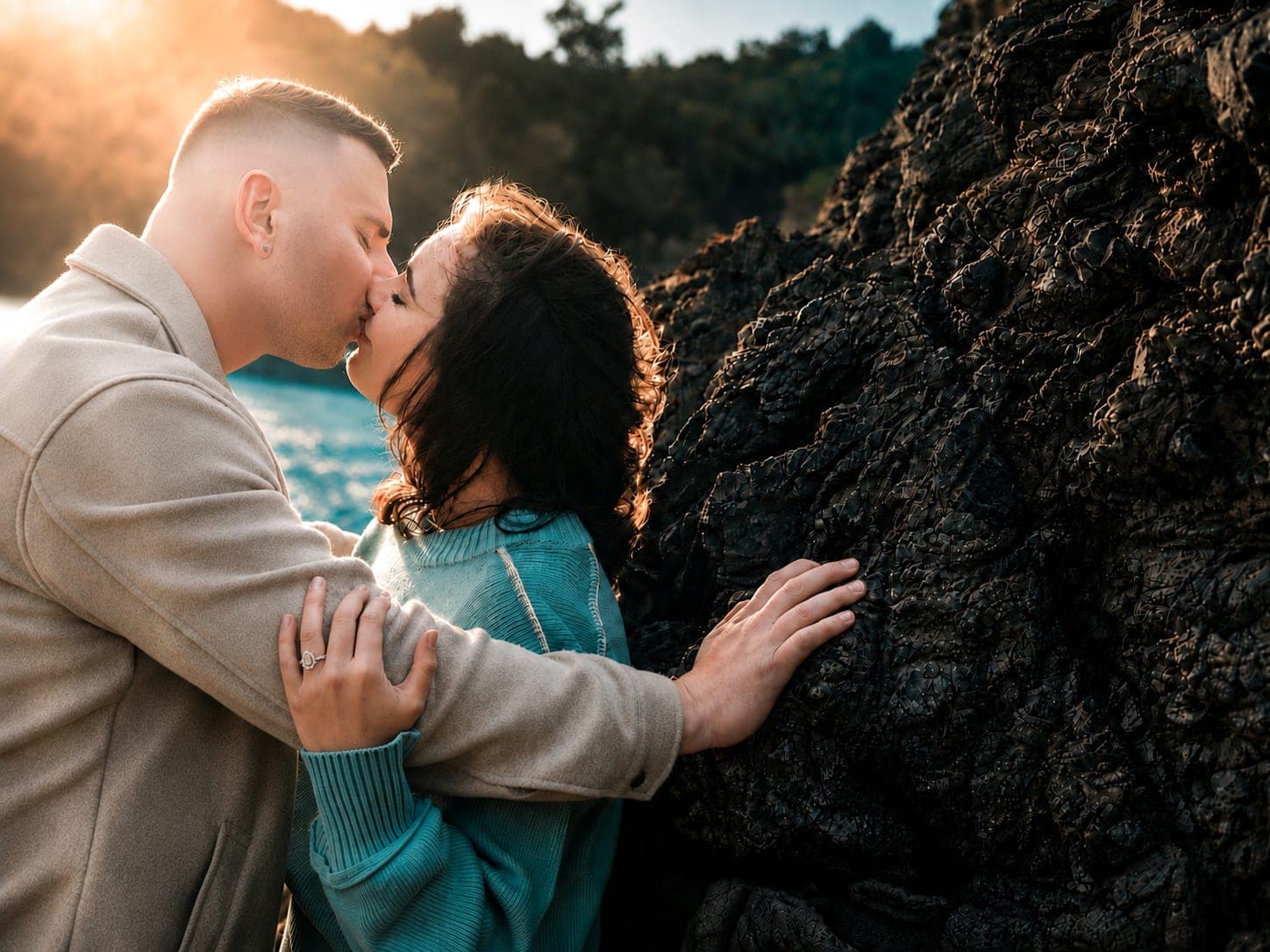 Couple kissing against dark rocks in warm sunset light
