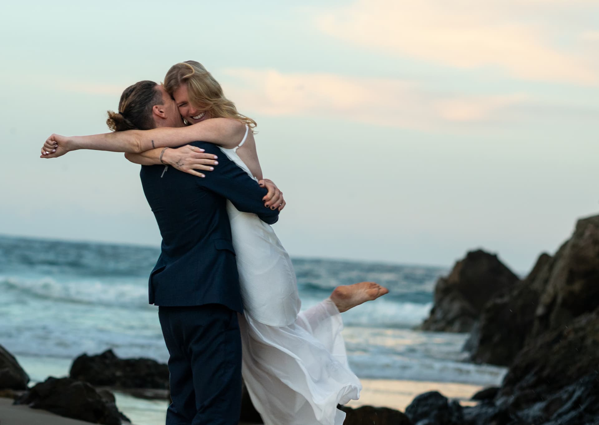 Groom lifting his bride into a joyful embrace above the rocks and sea