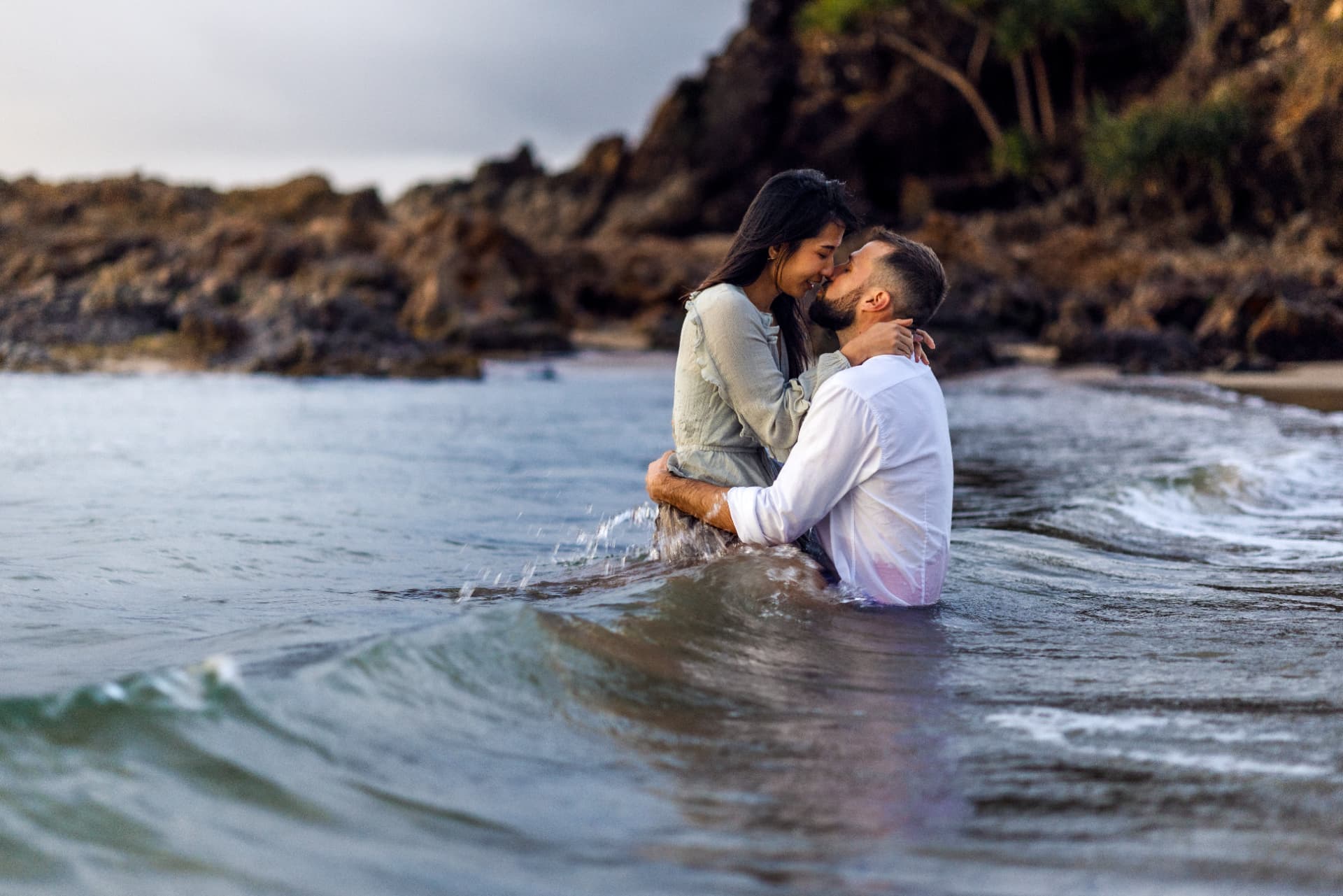 Couple embracing waist-deep in the ocean in front of the rocks