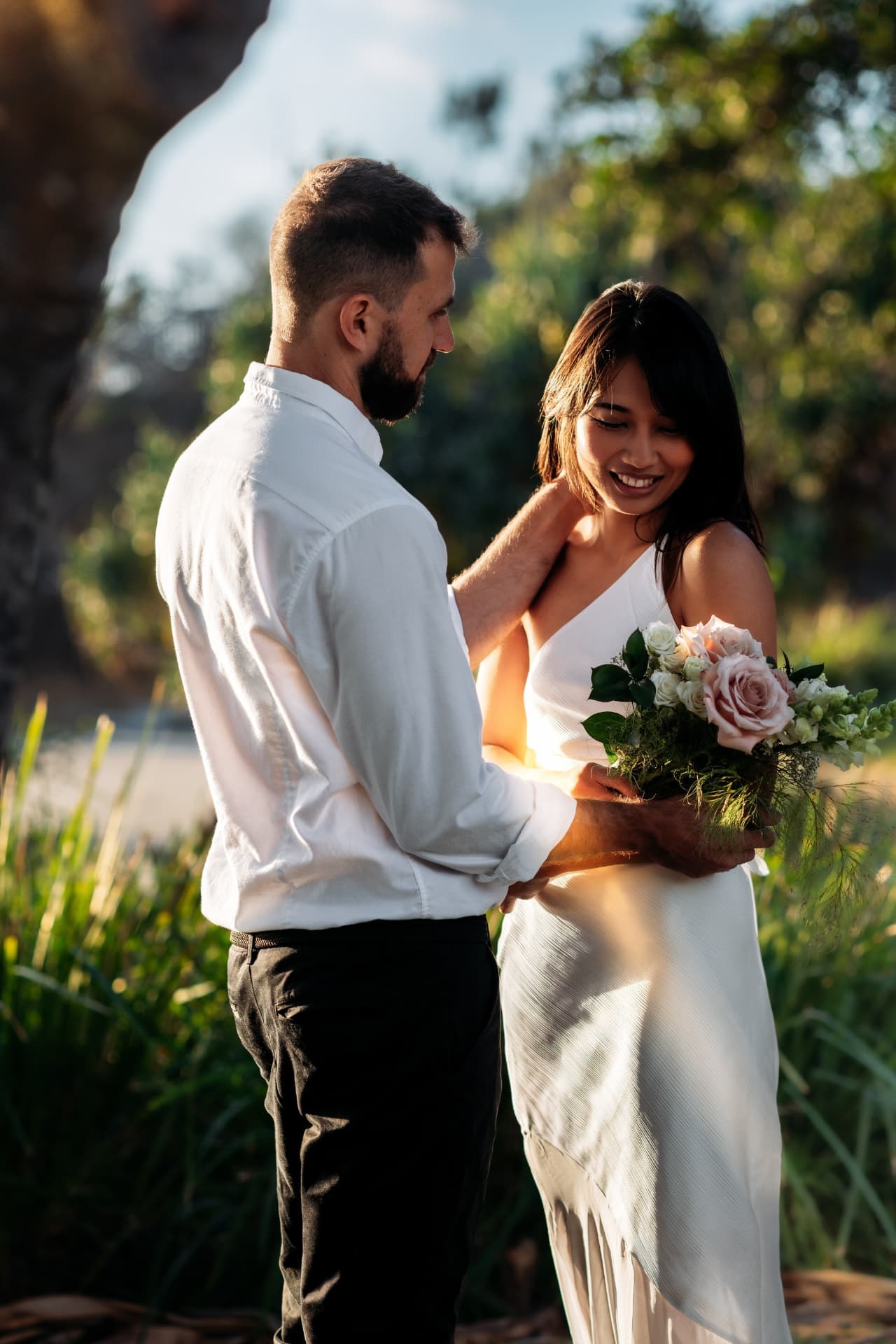 Bride resting on her groom's shoulder beneath pandanus trees at golden hour