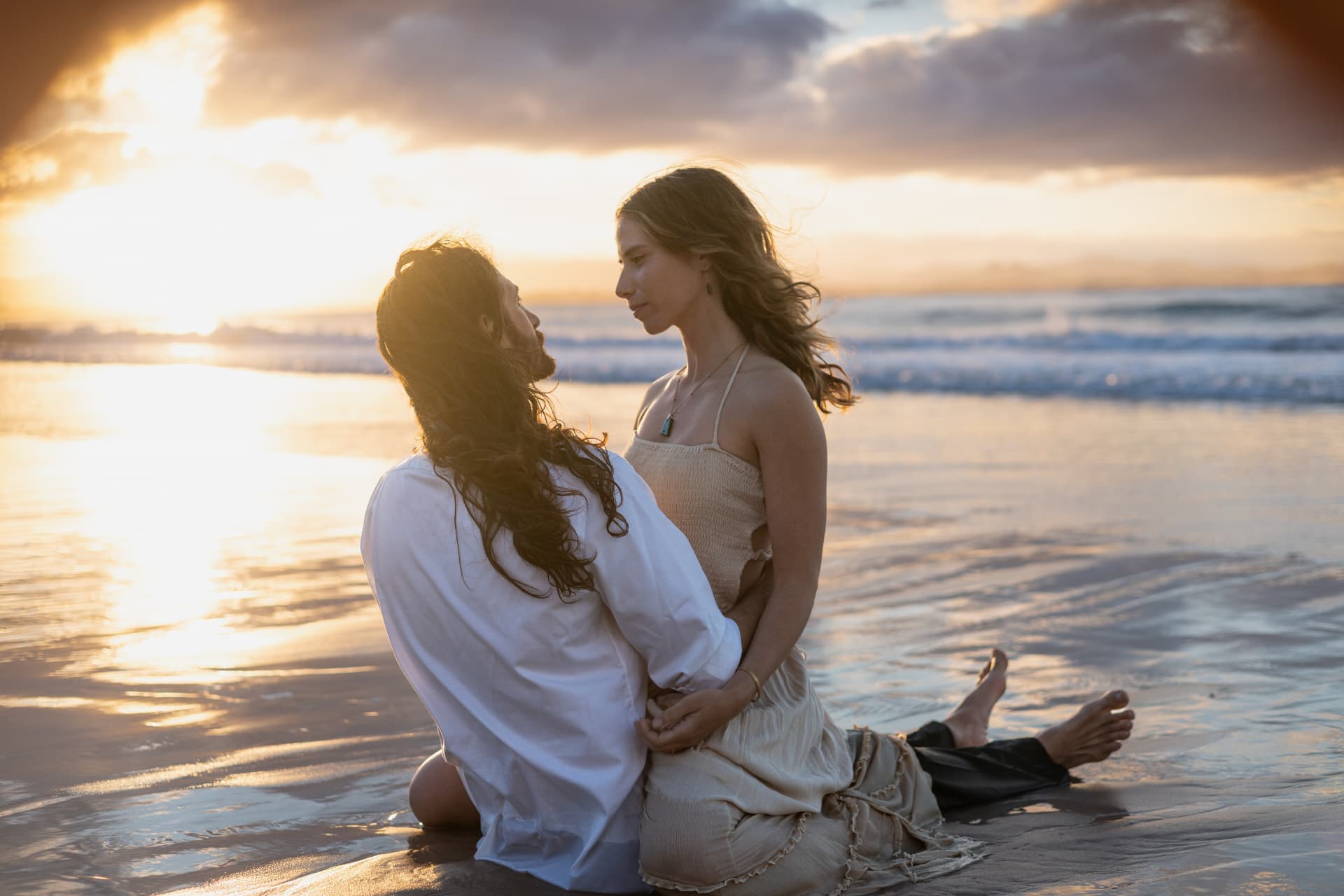 Couple kneeling together on the wet sand looking into the setting sun