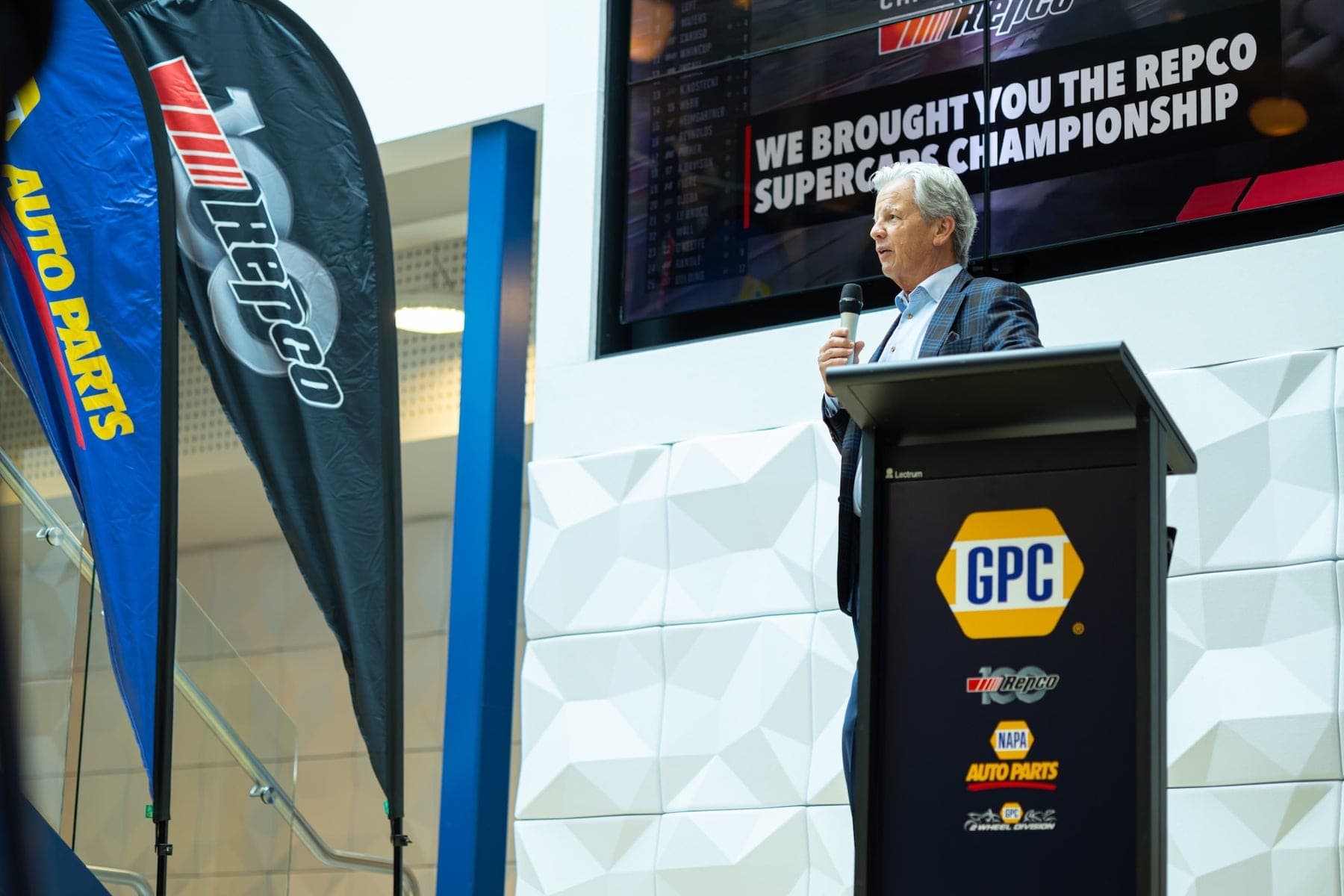 Speaker at a GPC-branded lectern beside a Repco banner