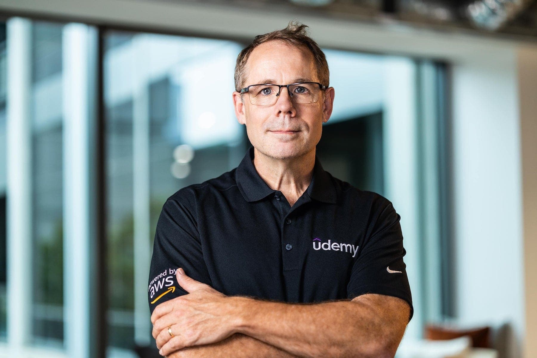 Man in a Udemy polo with arms crossed in an office