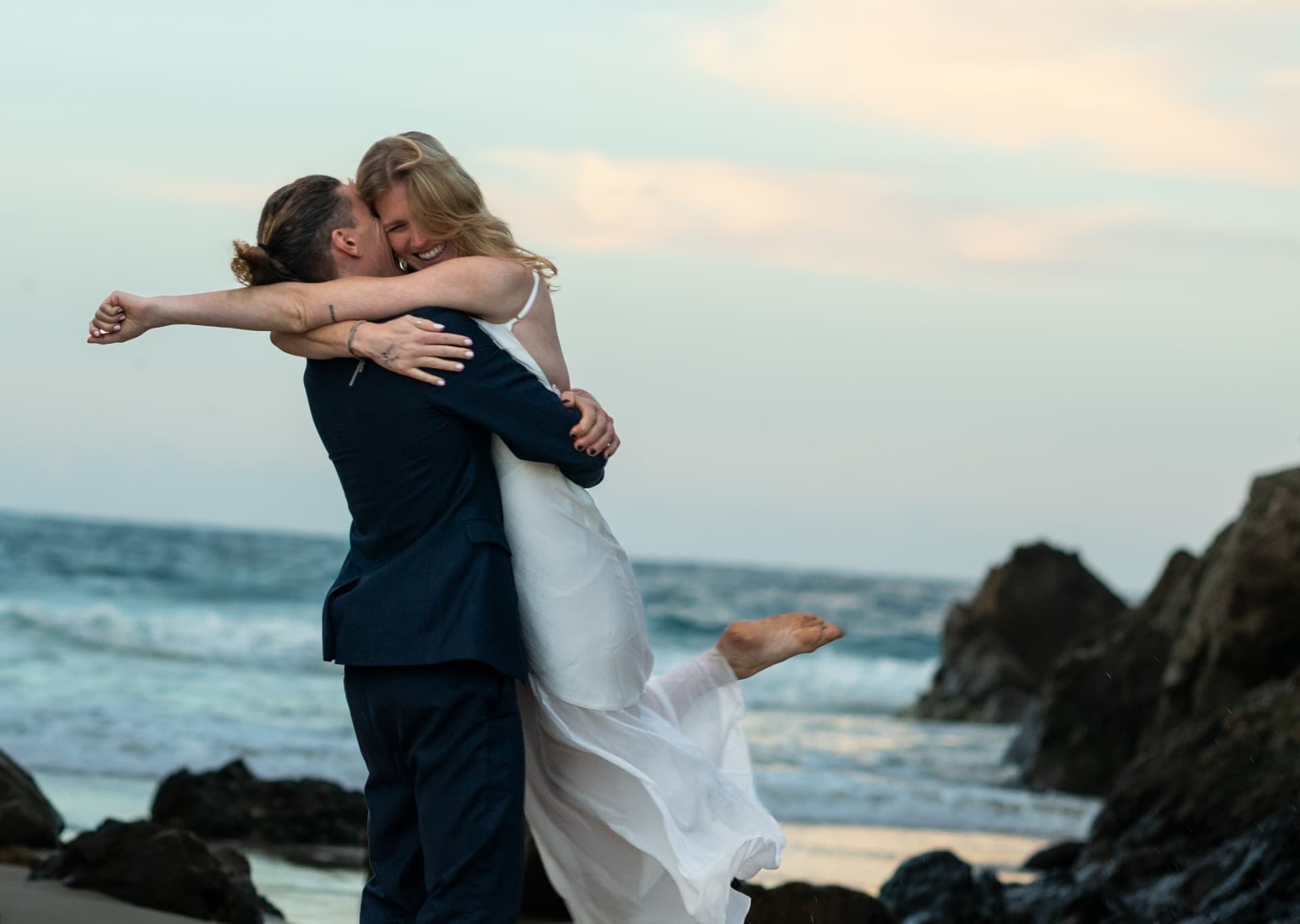 Groom lifting the bride on the sand as waves roll in
