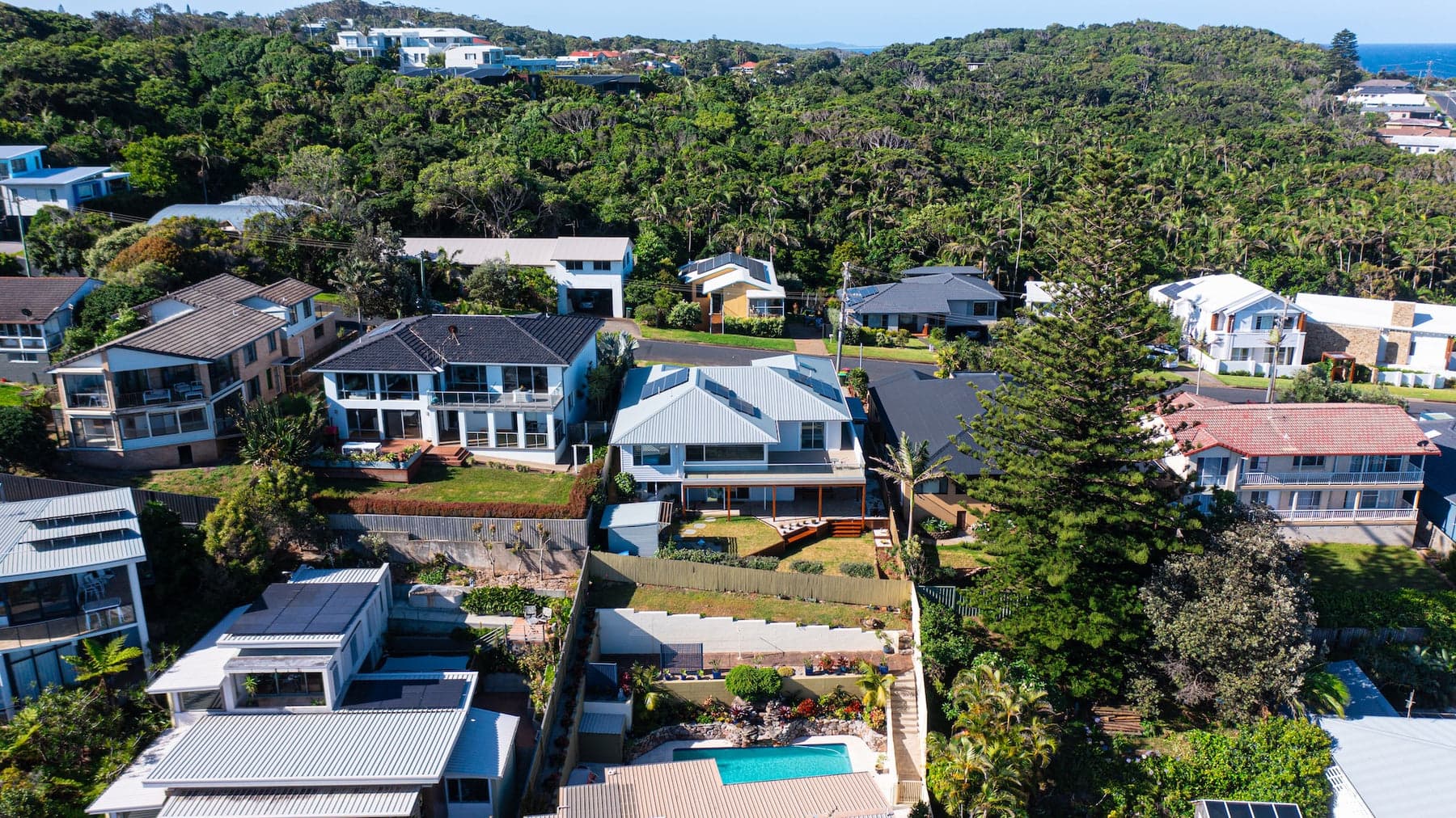 Aerial of terraced hillside homes with a backyard pool among tall pines