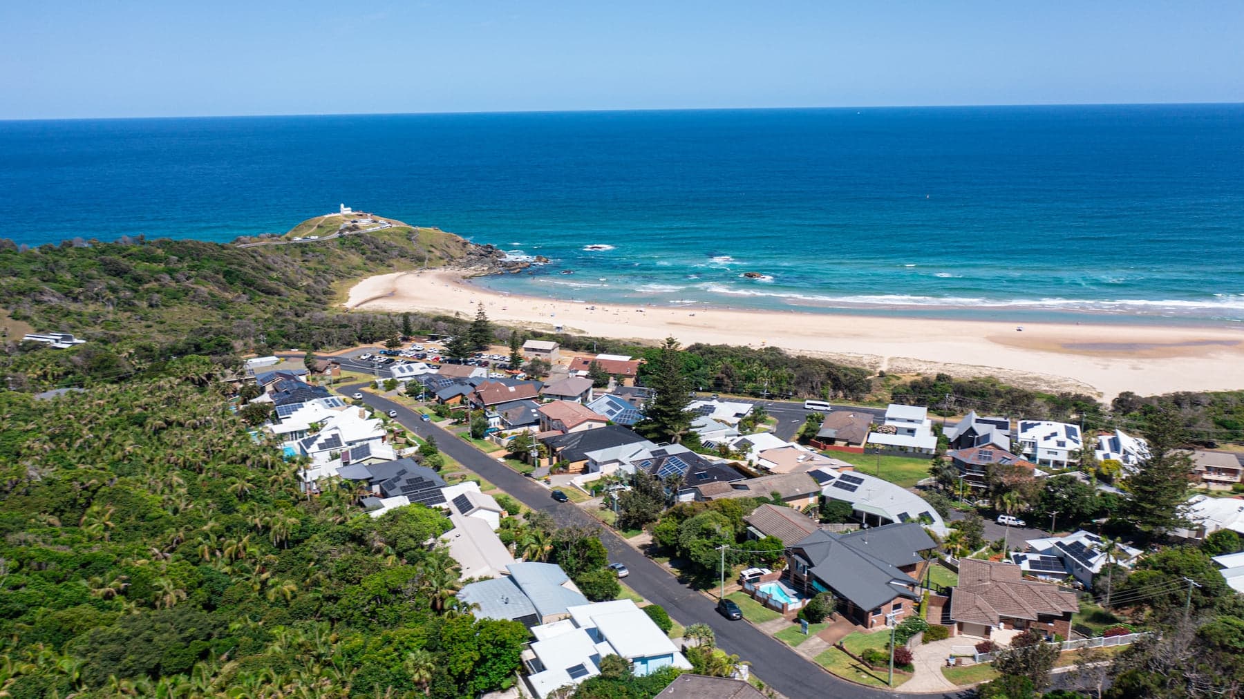Aerial of a coastal suburb, sandy beach and lighthouse headland