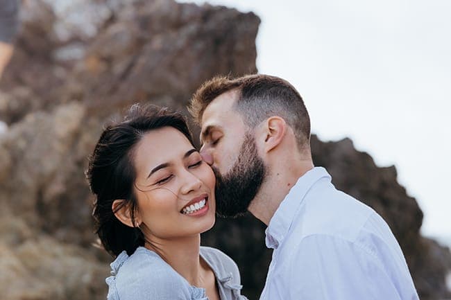 Mario kissing Aris on the cheek as she smiles with eyes closed