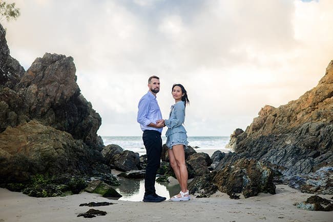 Wide view of the couple standing between rocky outcrops on the sand