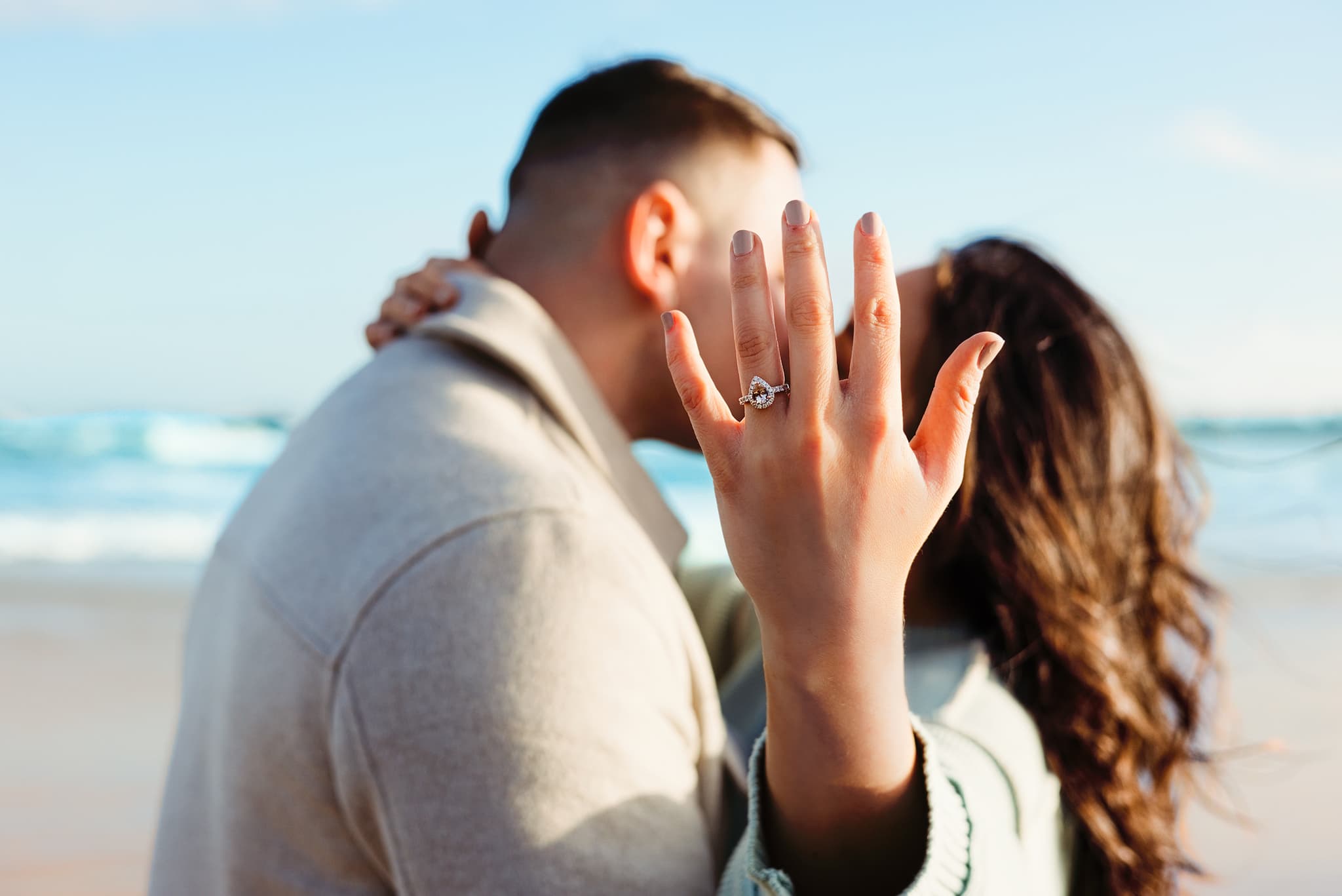 Tia showing her engagement ring to camera while kissing Joseph on the beach