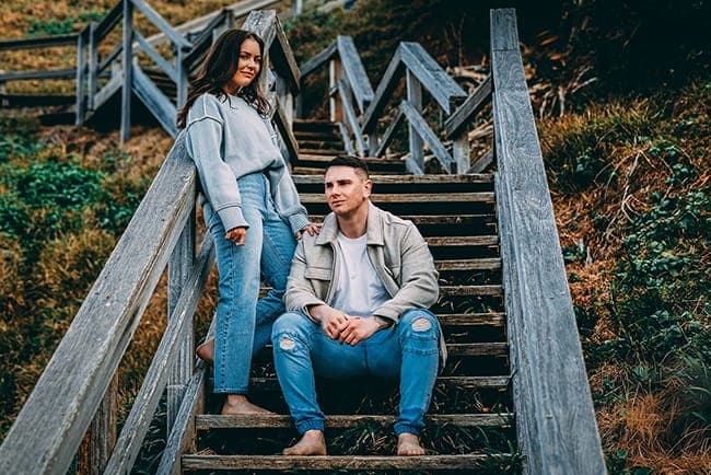 Joseph and Tia sitting together on weathered timber beach stairs