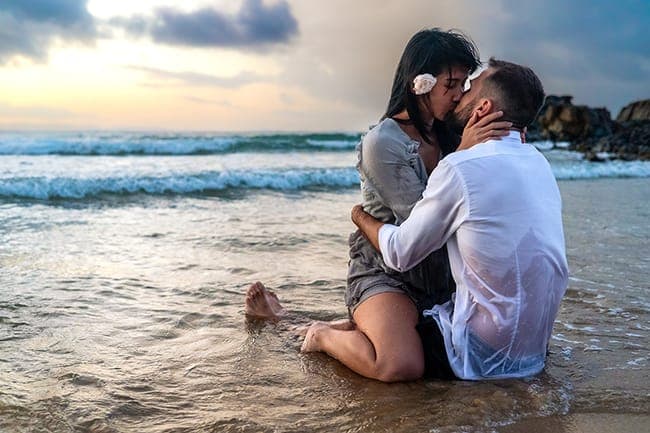 Couple kissing in the shallows under a soft sunset sky