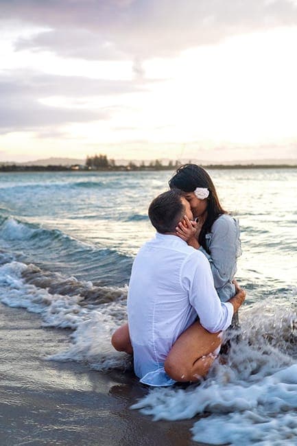 Couple embracing as small waves wash around them at dusk