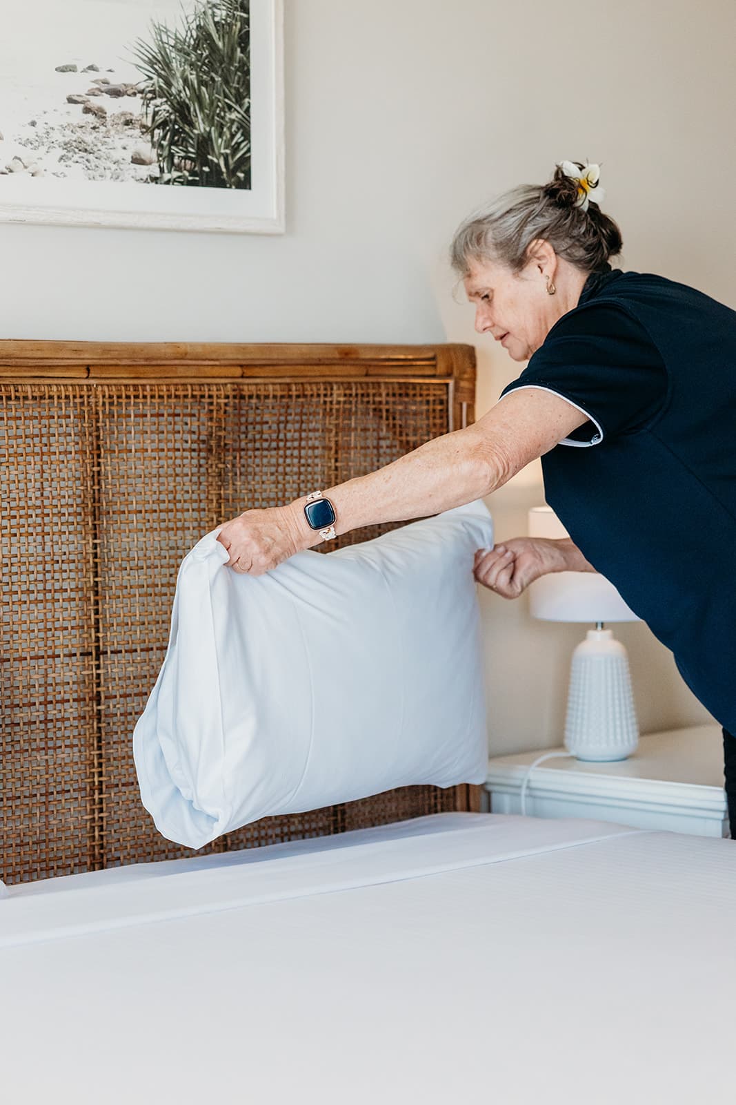 Housekeeper plumping a pillow on a freshly made bed