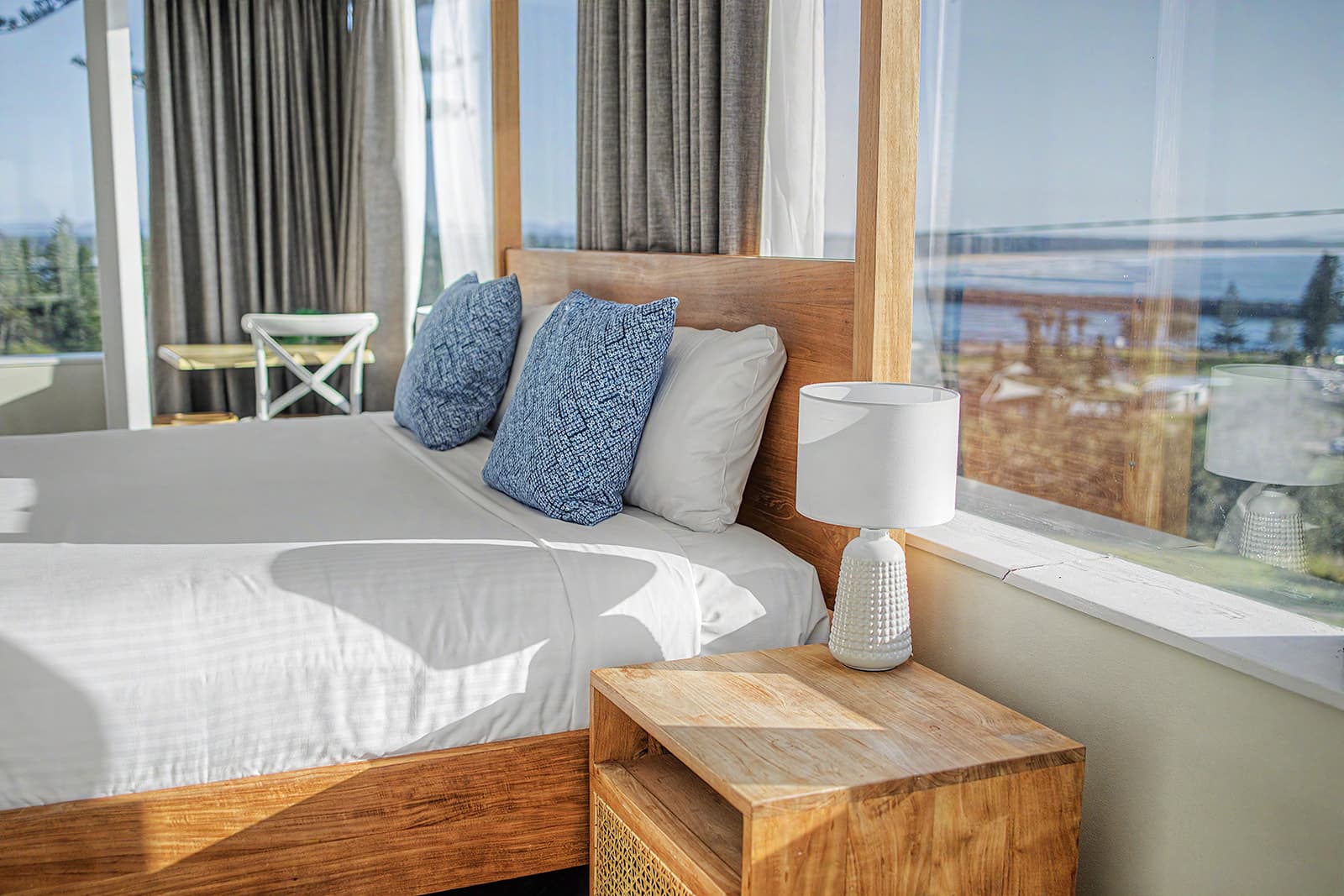 Sunlit timber four-poster bed with blue cushions and water views through the window