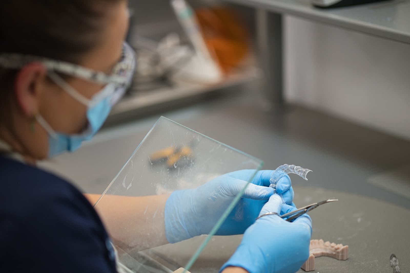 Gloved technician trimming a clear aligner in the lab