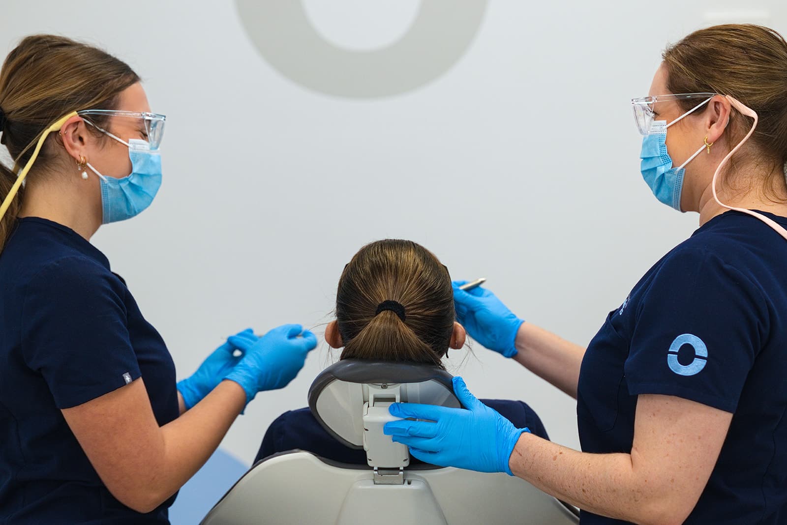 Two gloved clinicians treating a patient in the chair
