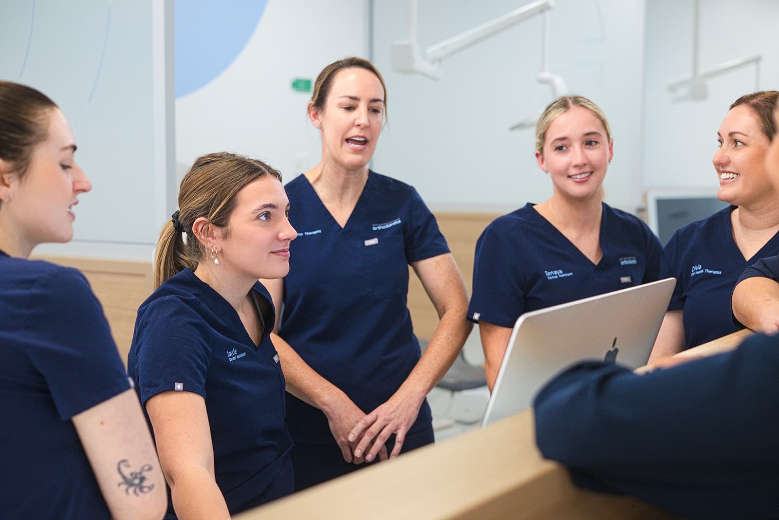 Dental assistants in navy scrubs chatting together around a computer