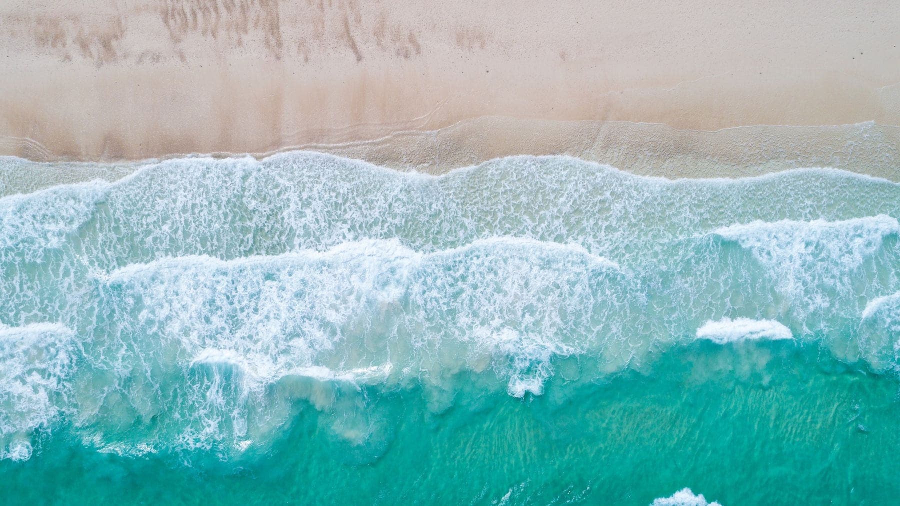 Top-down aerial of turquoise waves meeting the sand