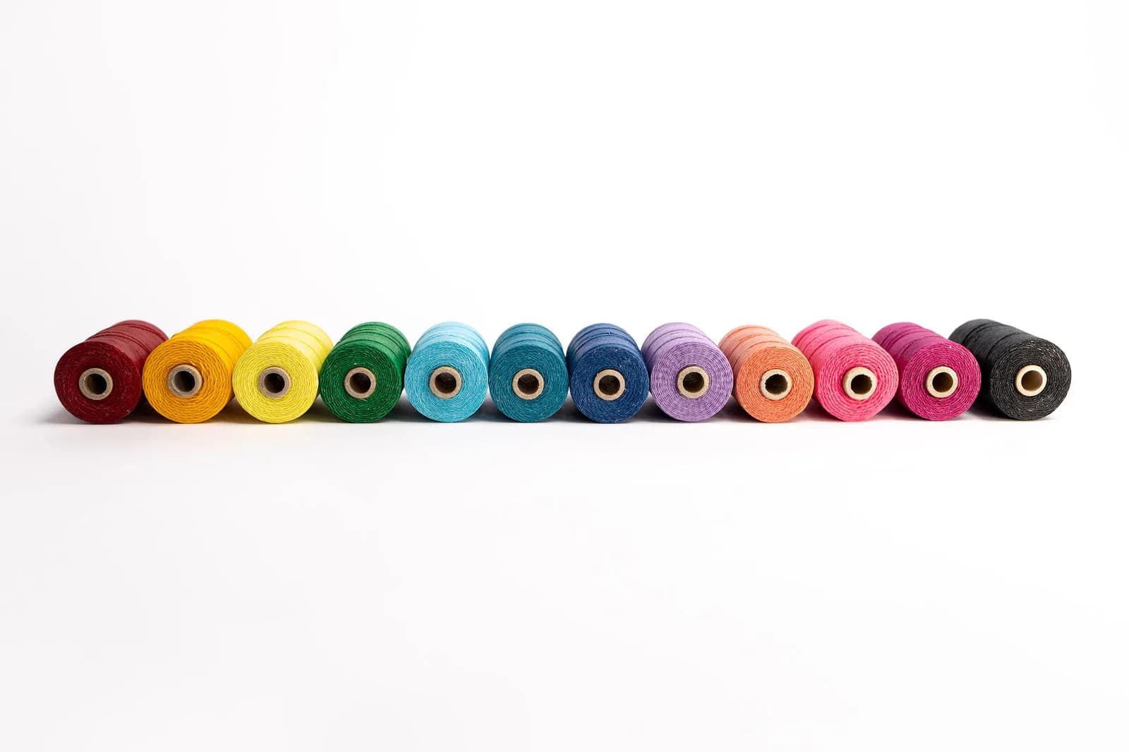 Row of rainbow thread spools on a white background