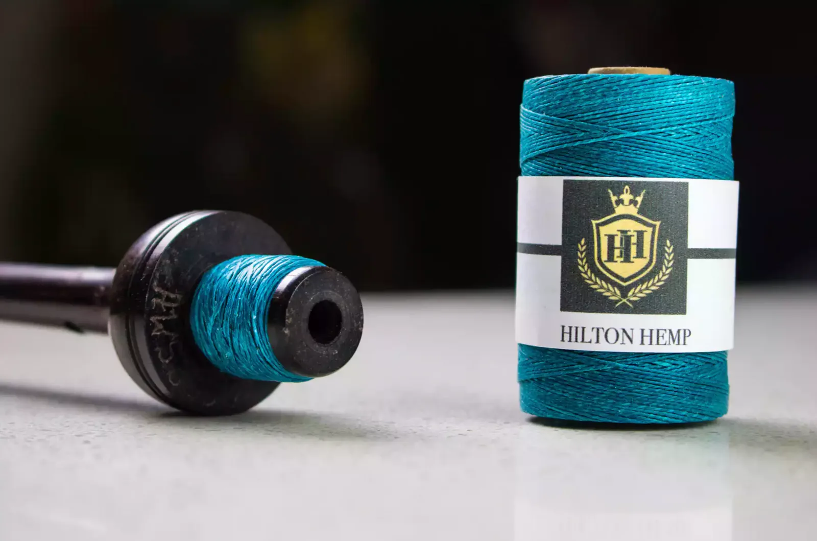 Teal thread spool with a branded label beside a dark spool