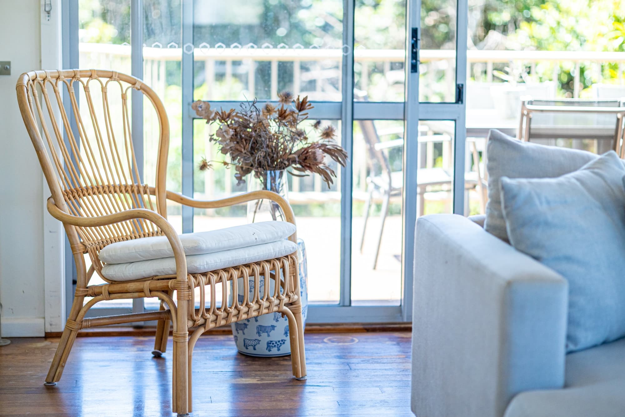 Rattan armchair and dried flowers beside sliding doors to a deck