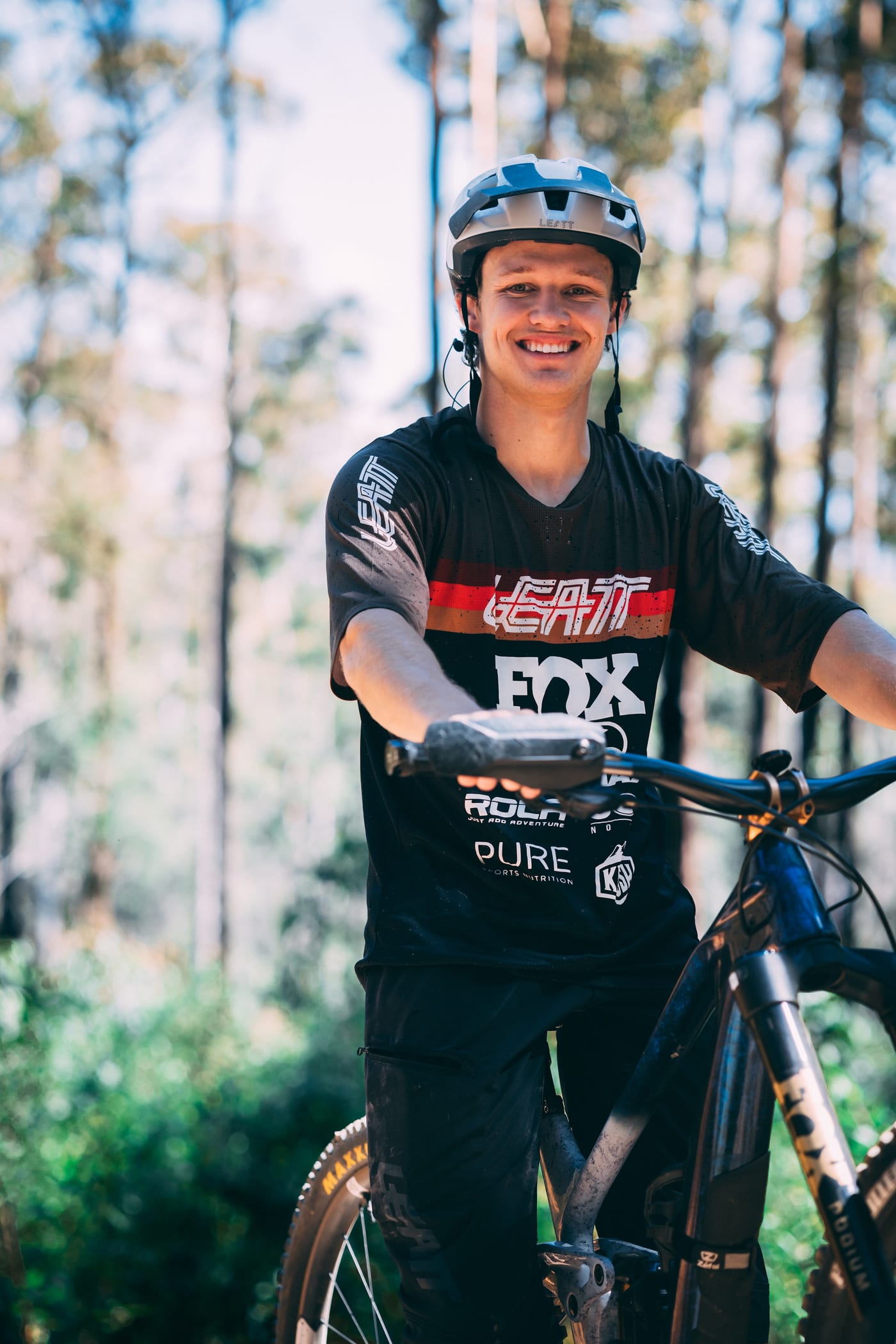 Tom Jenkins in his Leatt helmet, grinning with a hand on the handlebars