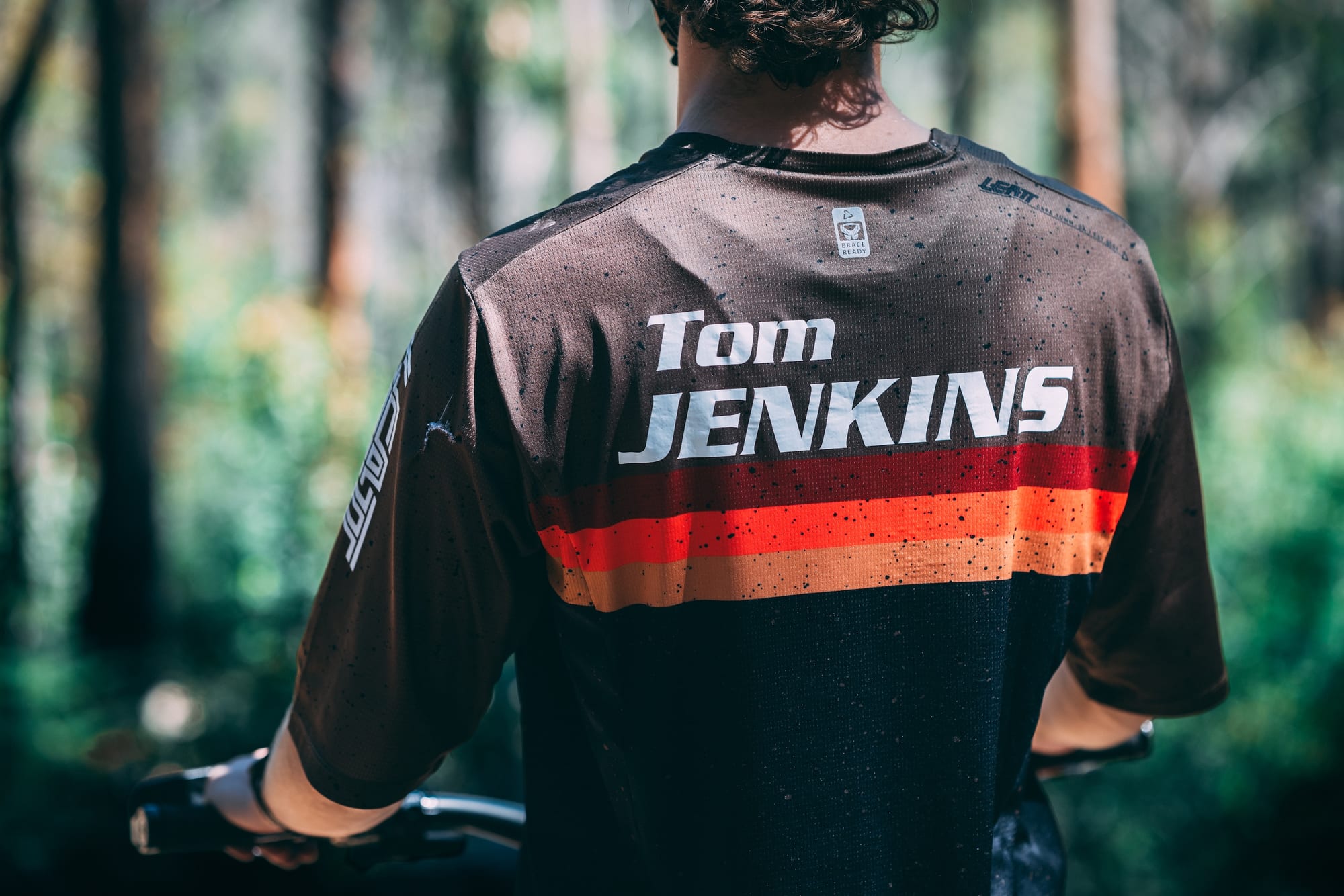 Back of Tom Jenkins' custom riding jersey with his name across the shoulders, forest behind